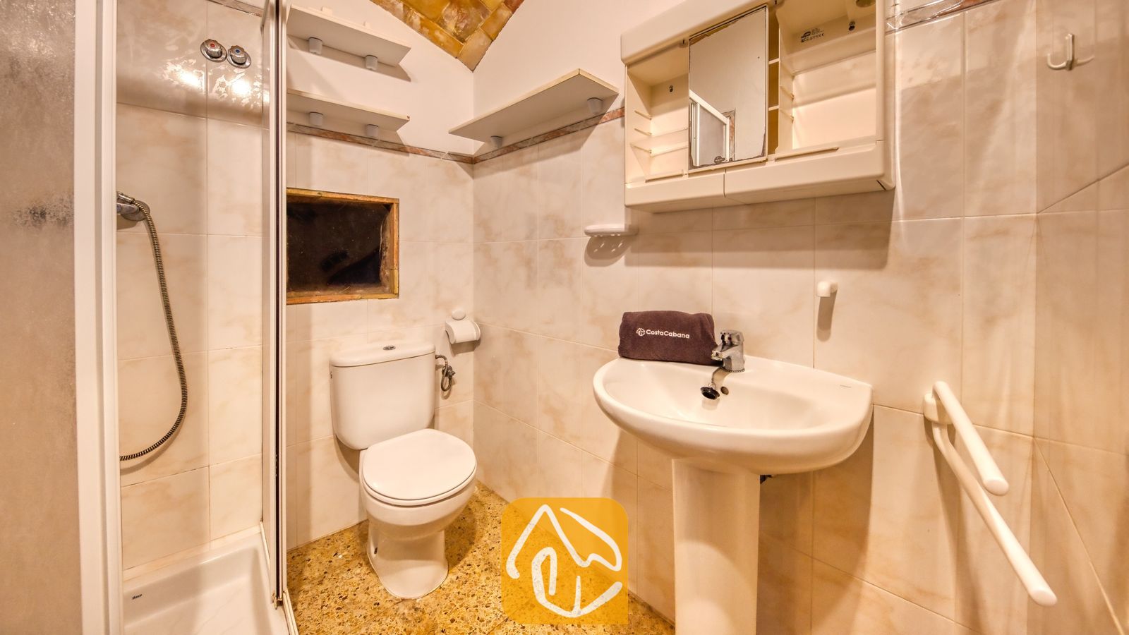 Vakantievilla's Costa Brava Countryside Spanje - Villa Can Bernardi - Compacte badkamer met beige betegelde muren, een witte wastafel op zuil met een opgevouwen handdoek, een toilet en een inloopdouche.
