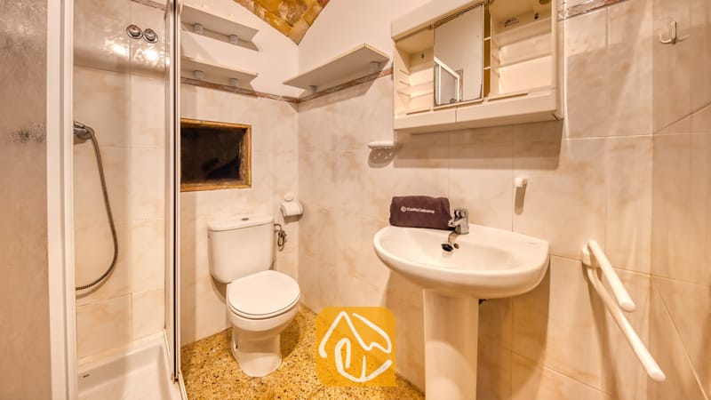 Villas de vacances Costa Brava Countryside Espagne - Villa Can Bernardi - Salle de bains compacte dotée de murs carrelés de beige, d'un lavabo sur pied blanc avec une serviette pliée, de toilettes et d'une cabine de douche fermée.