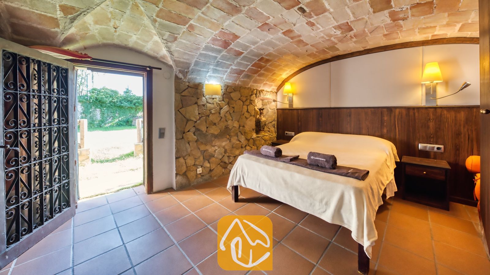 Vakantievilla's Costa Brava Countryside Spanje - Villa Can Bernardi - Slaapkamer met een karakteristiek gewelfd stenen plafond, accenten van natuurlijke muren en een open doorgang naar een buitentuin.