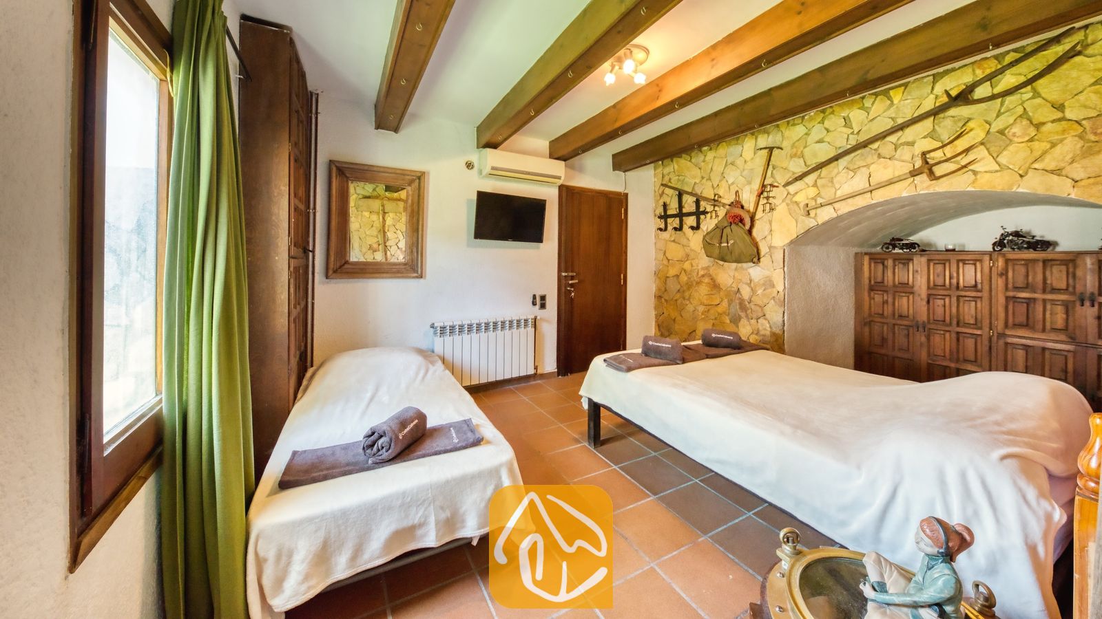 Vakantievilla's Costa Brava Countryside Spanje - Villa Can Bernardi - Slaapkamer met twee eenpersoonsbedden, authentieke houten plafondbalken en een natuurstenen accentmuur in Villa Can Bernardi