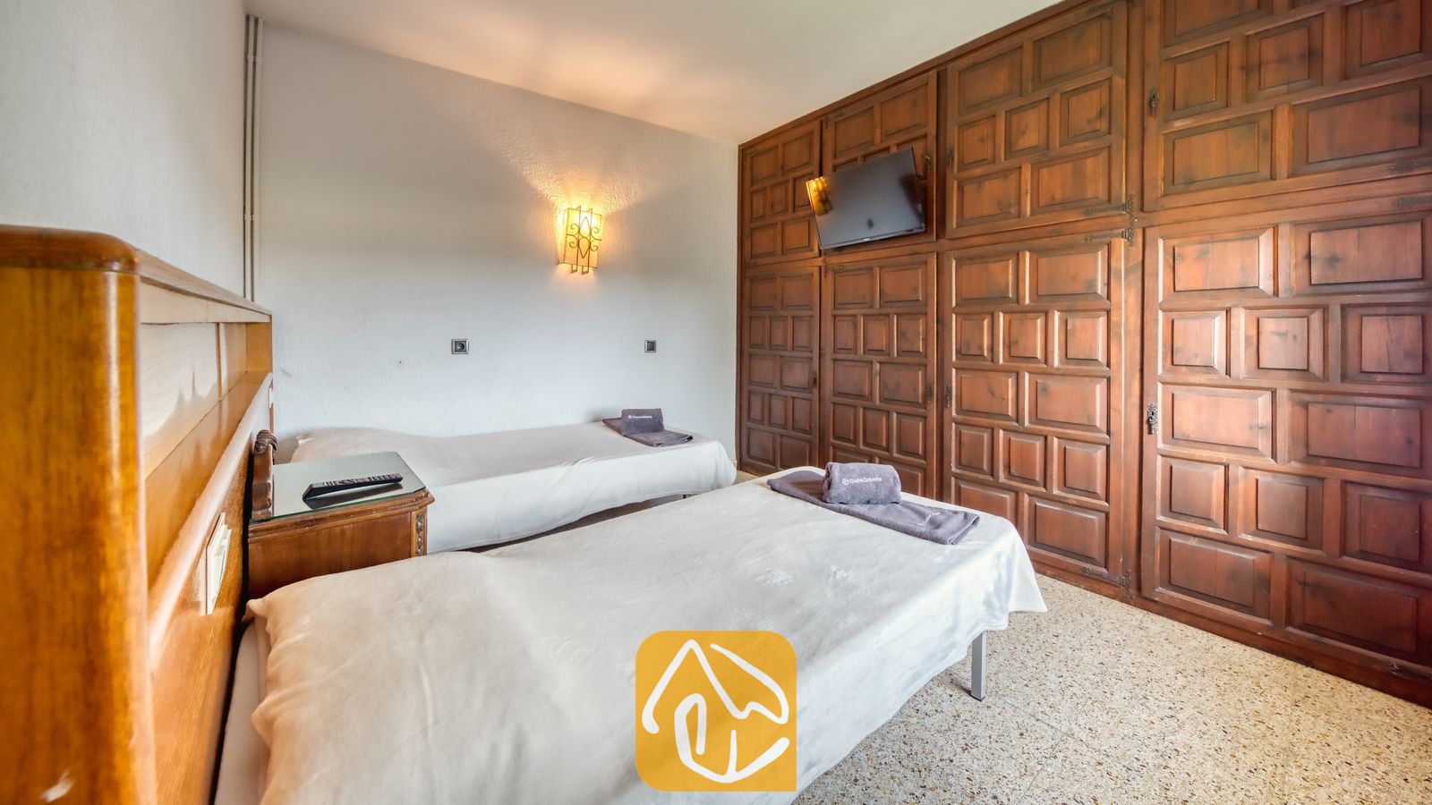 Vakantievilla's Costa Brava Countryside Spanje - Villa Can Bernardi - Slaapkamer met twee eenpersoonsbedden, een grote kledingkastwand van donker hout, een aan de muur bevestigde televisie en een tegelvloer.