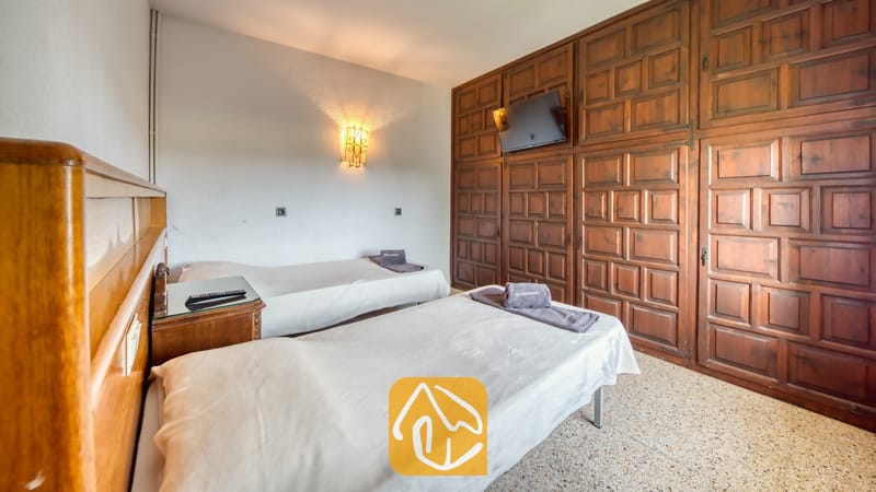 Villas de vacances Costa Brava Countryside Espagne - Villa Can Bernardi - Chambre avec deux lits simples, un grand mur de placards en bois sombre, une télévision murale et un sol carrelé.