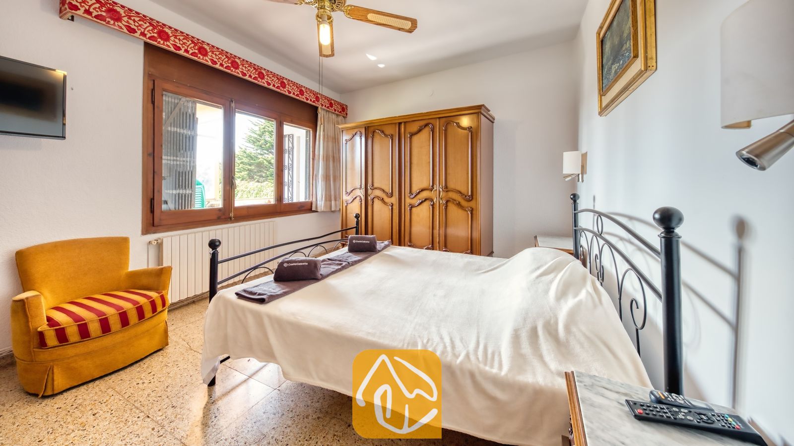 Vakantievilla's Costa Brava Countryside Spanje - Villa Can Bernardi - Slaapkamer met een tweepersoonsbed met metalen frame, een donkere houten kledingkast en een gele fauteuil met gestreept kussen bij Villa Can Bernardi