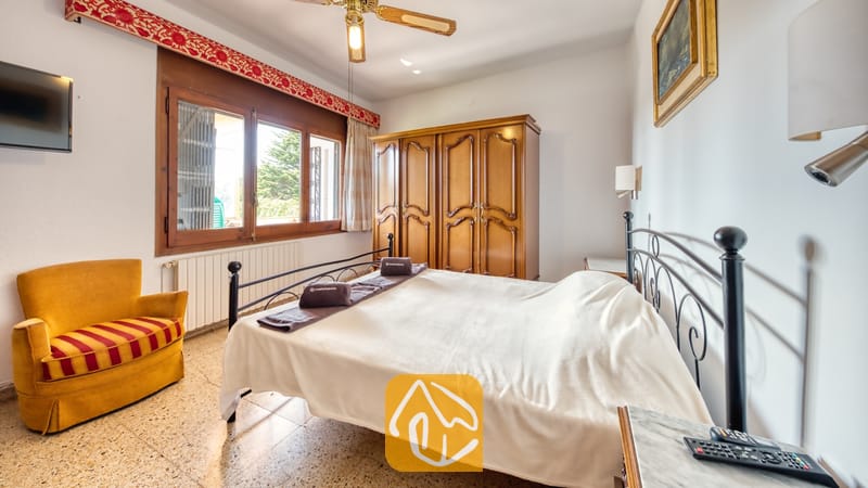 Villas de vacances Costa Brava Countryside Espagne - Villa Can Bernardi - Chambre avec un lit double en fer forgé, une armoire en bois foncé et un fauteuil jaune doté d'un coussin à rayures à la Villa Can Bernardi