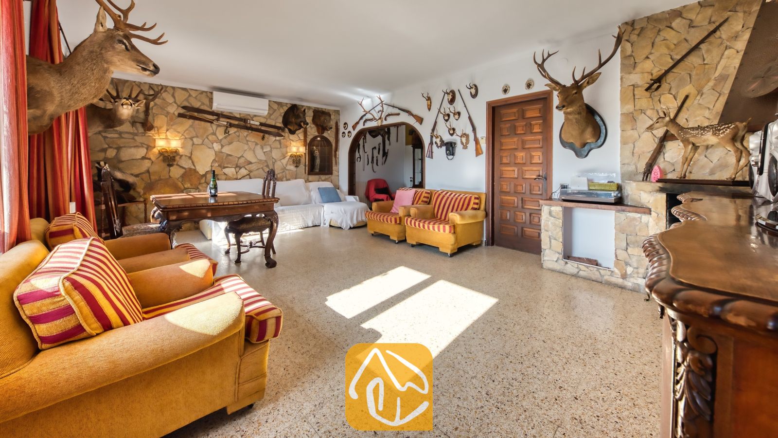 Vakantievilla's Costa Brava Countryside Spanje - Villa Can Bernardi - Woonkamer voorzien van geel gestreepte fauteuils, stenen muren en opgezette dieren.