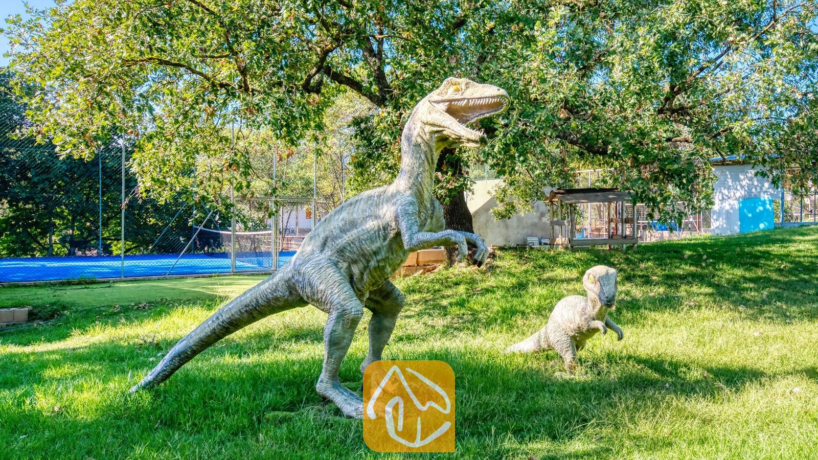 Vakantievilla's Costa Brava Countryside Spanje - Villa Can Bernardi - Grote dinosaurustandbeelden op een groen grasveld bij Villa Can Bernardi, met een tennisbaan en bomen zichtbaar op de achtergrond.