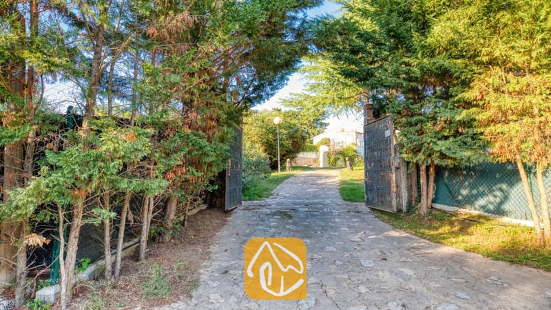 Villas de vacances Costa Brava Countryside Espagne - Villa Can Bernardi - Allée pavée de pierres encadrée de grands arbres verdoyants et de portails métalliques ouverts menant à l'entrée de la Villa Can Bernardi