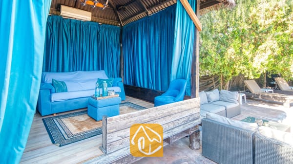 Vakantievilla's Costa Brava Countryside Spanje - Villa Can Bernardi - Overdekte buitenlounge bij Villa Can Bernardi, voorzien van helderblauwe gordijnen, een bijpassende blauwe bank en een vloerkleed met patroon.
