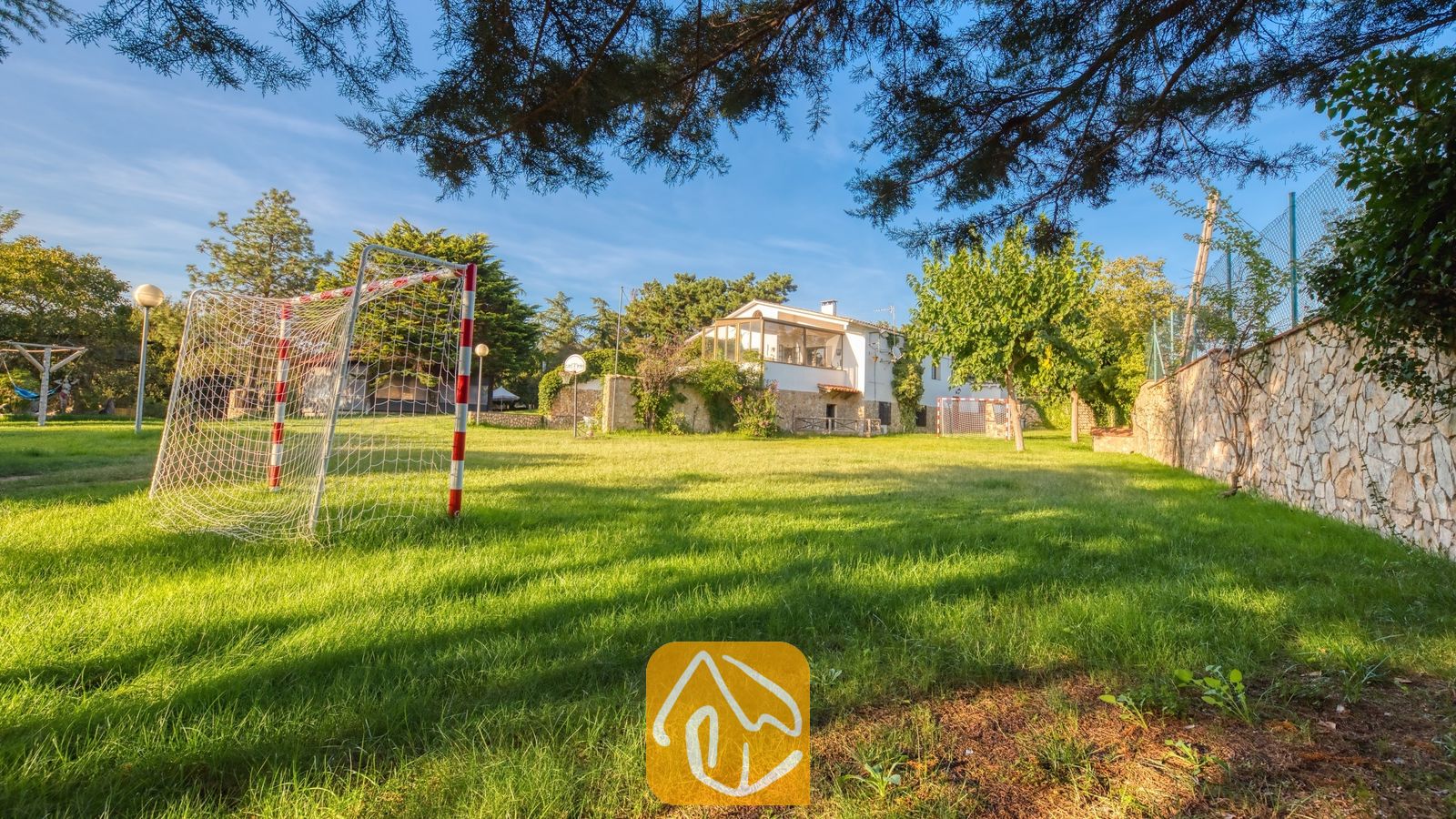 Vakantievilla's Costa Brava Countryside Spanje - Villa Can Bernardi - Groot groen grasveld met een rood-wit voetbaldoel bij Villa Can Bernardi, omzoomd door een stenen muur en bomen.
