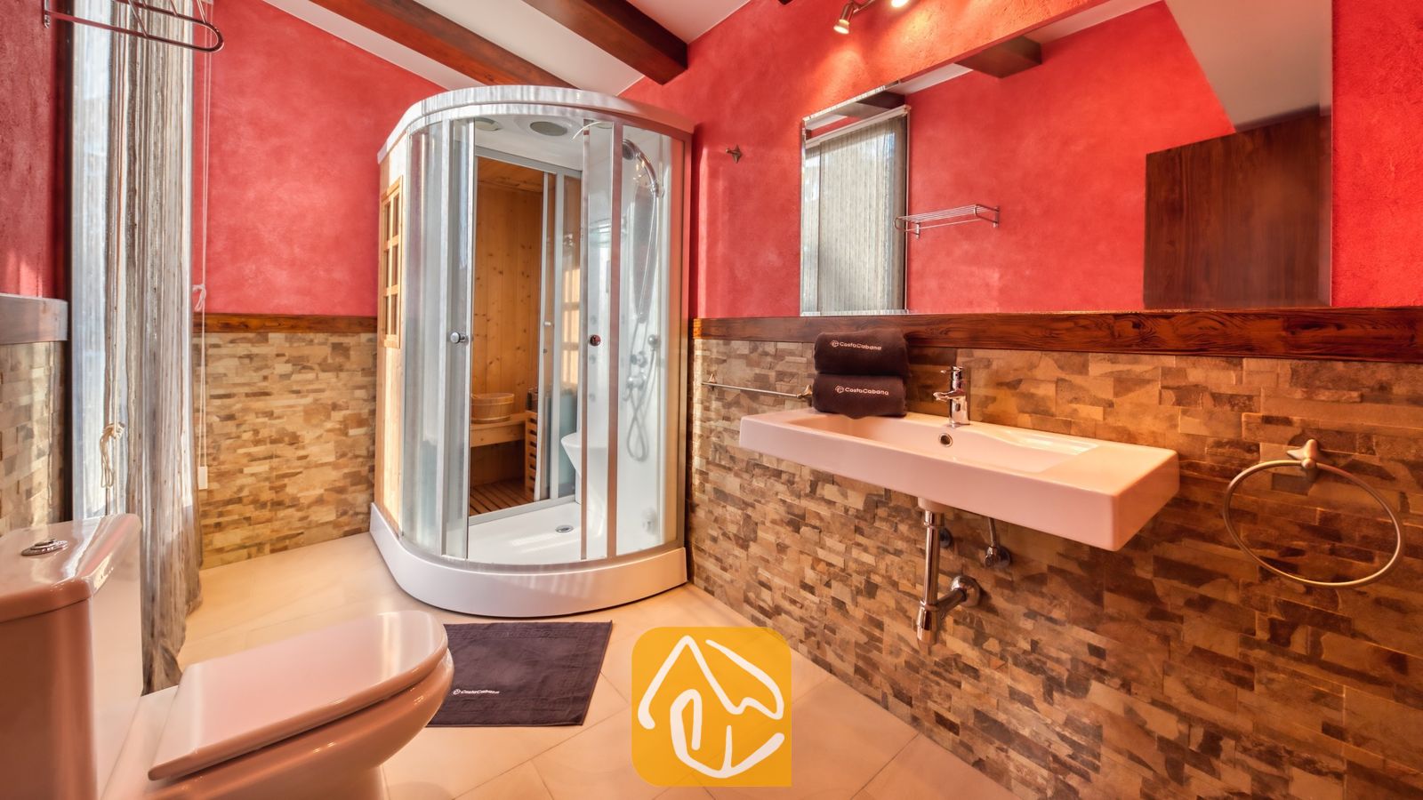 Vakantievilla's Costa Brava Countryside Spanje - Villa Can Bernardi - Badkamer met een gebogen glazen douchecabine met houten saunainterieur, een witte wandwastafel en muren van rode en natuurstenen tegels.
