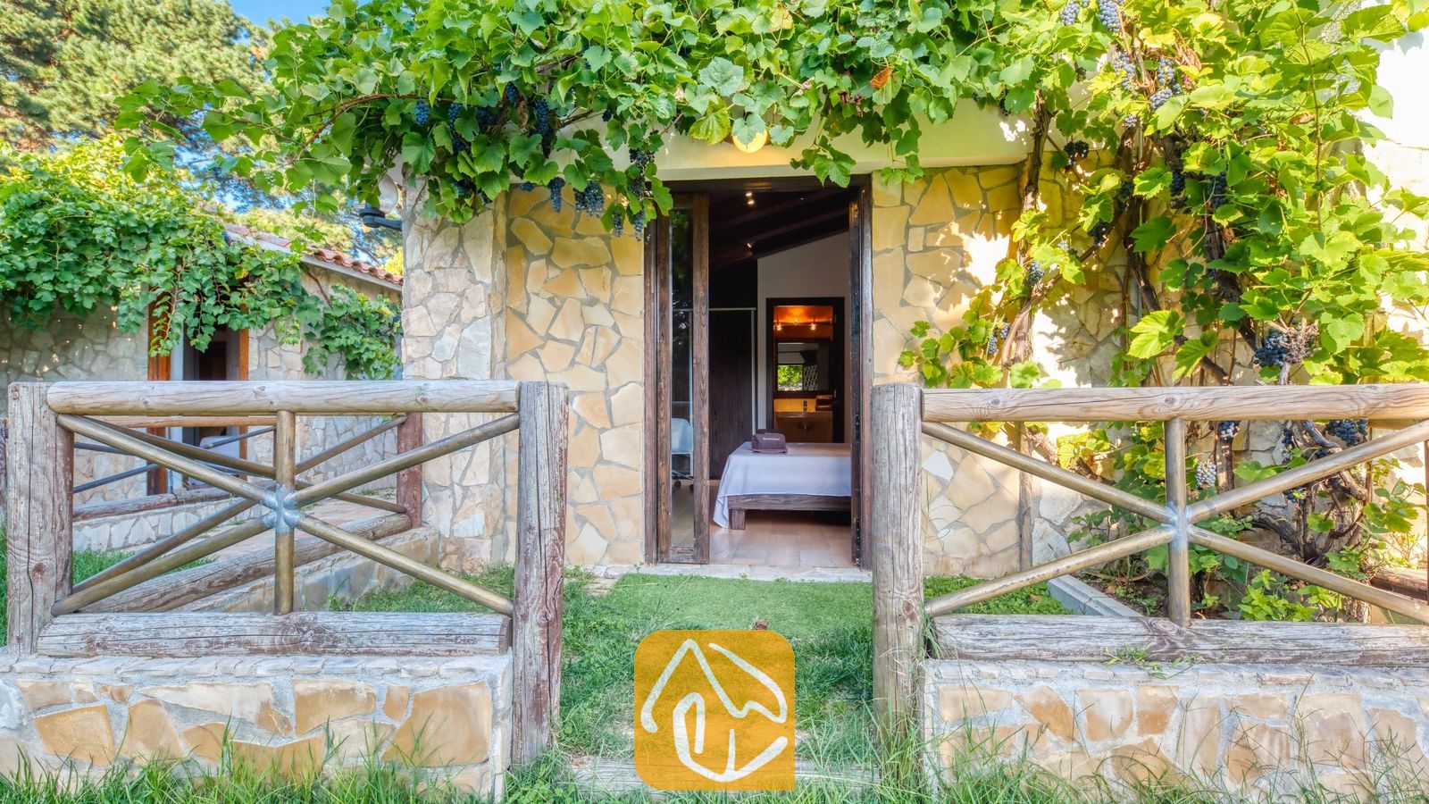 Vakantievilla's Costa Brava Countryside Spanje - Villa Can Bernardi - De buitenentree van Villa Can Bernardi, om lijst door stenen muren en groene wijnranken met donkere druiven, leidt naar een slaapkamer met een houten bed.