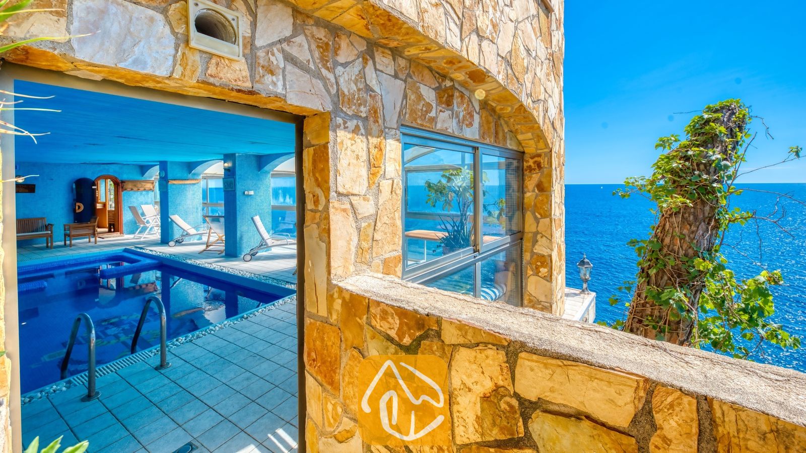 Vakantievilla's Costa Brava Spanje - Villa Infinity - Binnenzwembad bij Villa Infinity met blauwe tegelvloer, grote glazen ramen en stenen bogen met uitzicht op de oceaan.