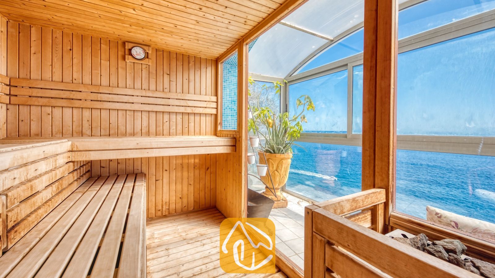Vakantievilla's Costa Brava Spanje - Villa Infinity - Interieur van een houten sauna met getrapte cederhouten banken, een wandthermometer en grote glazen ramen met uitzicht op de blauwe zee.