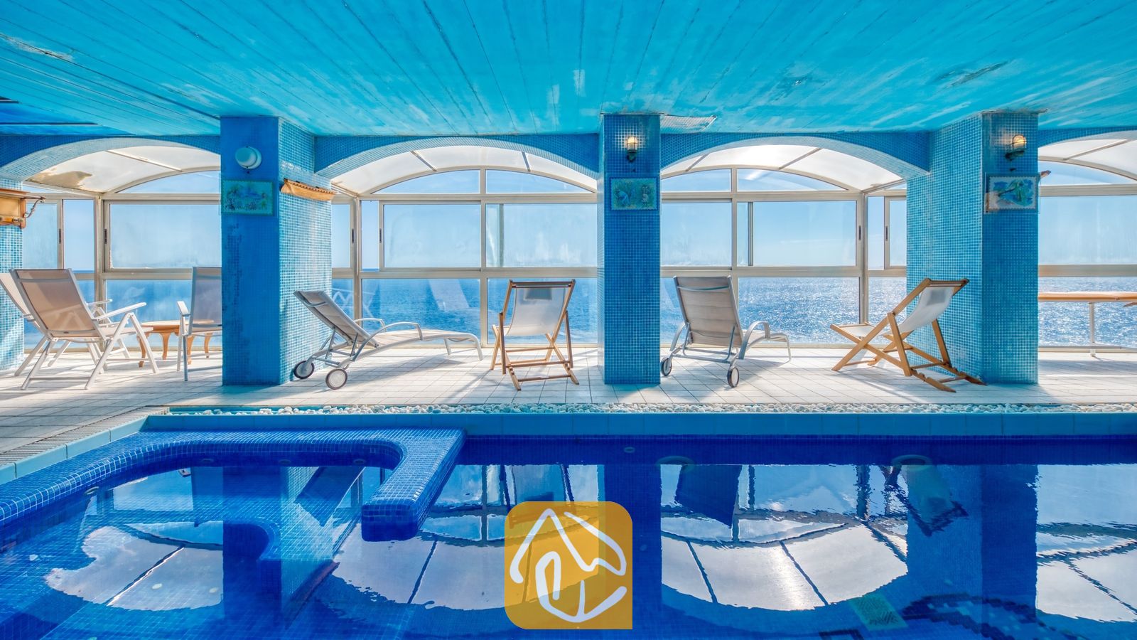 Vakantievilla's Costa Brava Spanje - Villa Infinity - Binnenzwembad en ligbedden bij Villa Infinity met blauwe mozaïekzuilen, boogvormige ramen en direct uitzicht op zee.