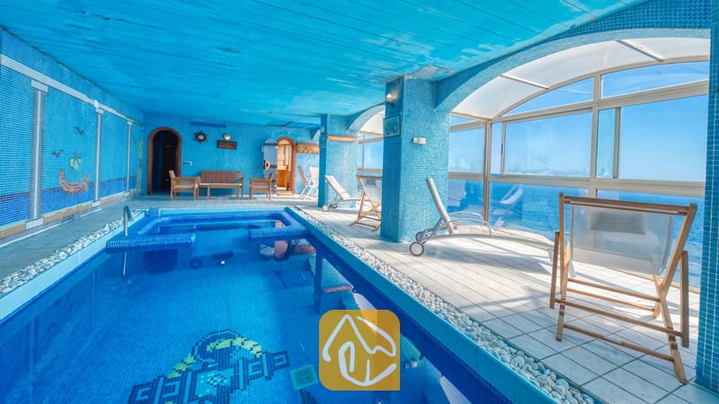 Villas de vacances Costa Brava Espagne - Villa Infinity - Piscine intérieure carrelée à la Villa Infinity, avec des murs en mosaïque bleue, des chaises longue blanches et de grandes baies vitrées surplombant la mer.