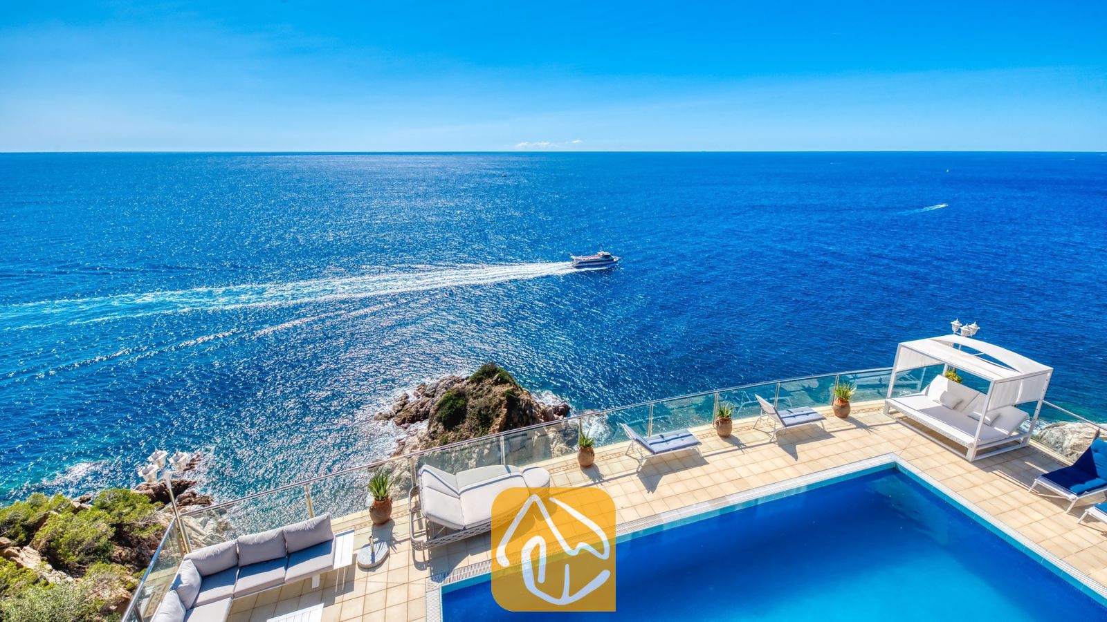 Vakantievilla's Costa Brava Spanje - Villa Infinity - Terras met uitzicht op zee bij Villa Infinity, voorzien van een zwembad, glazen balkonrailing, buitenbank, ligstoelen en een wit prieel.