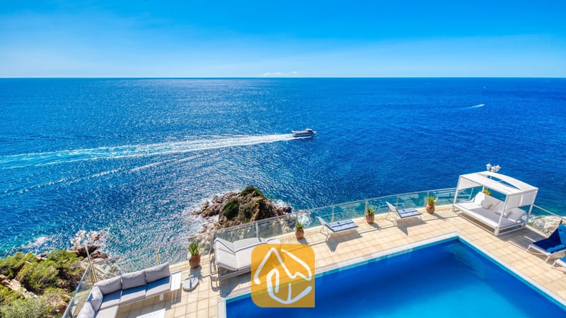 Vakantievilla's Costa Brava Spanje - Villa Infinity - Terras met uitzicht op zee bij Villa Infinity, voorzien van een zwembad, glazen balkonrailing, buitenbank, ligstoelen en een wit prieel.