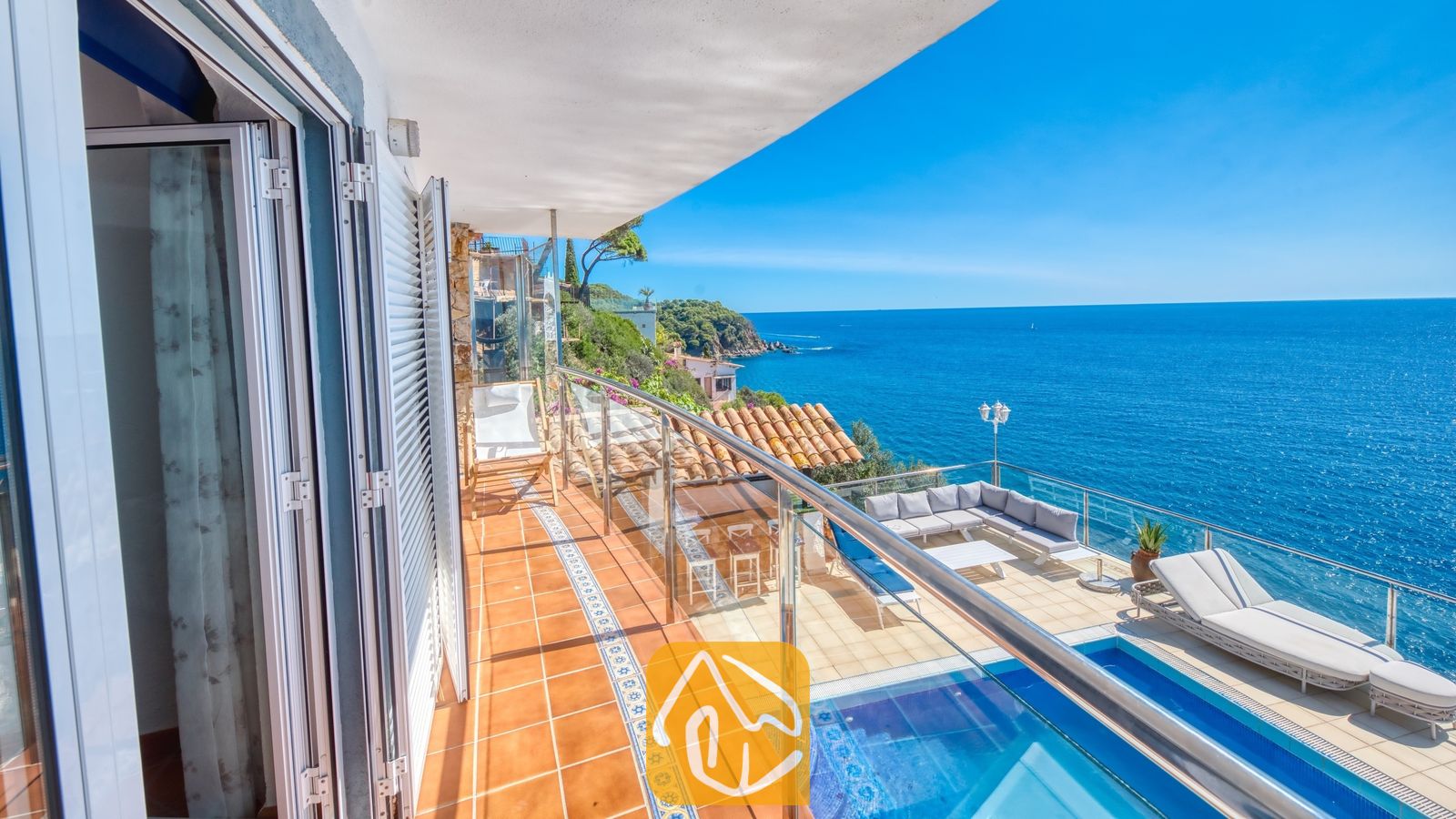 Vakantievilla's Costa Brava Spanje - Villa Infinity - Terras van Villa Infinity met terracotta tegelvloer, een glazen balustrade en een buiten zithoek met uitzicht op de blauwe zee.