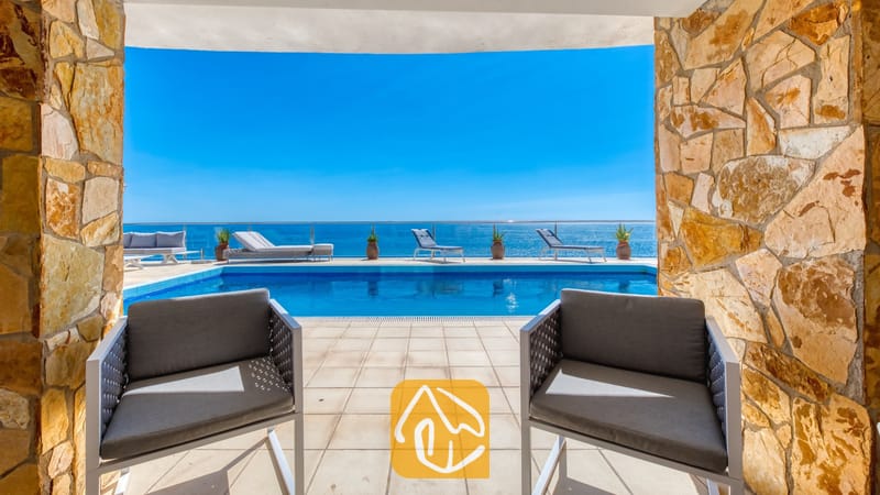 Vakantievilla's Costa Brava Spanje - Villa Infinity - Terras met uitzicht op een privézwembad en de zee door stenen pilaren bij Villa Infinity, voorzien van grijs gepositioneerde fauteuils en ligstoelen.
