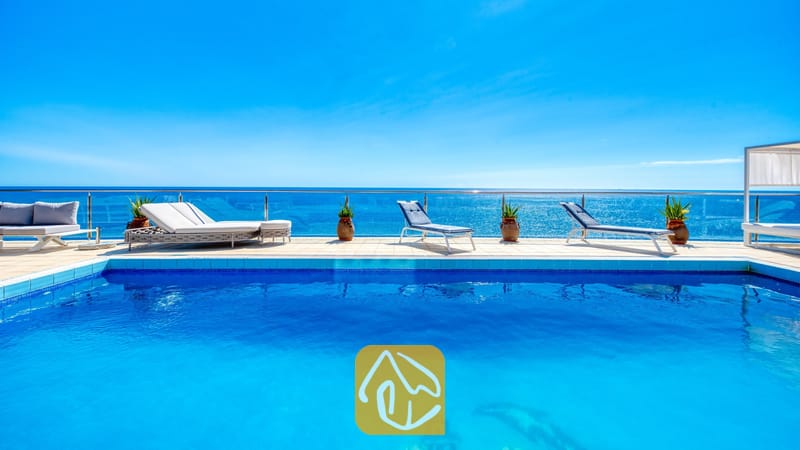 Vakantievilla's Costa Brava Spanje - Villa Infinity - Helblauwe zwembad bij Villa Infinity met witte ligbedden en potplanten op het betegelde zwembadterras met uitzicht op zee