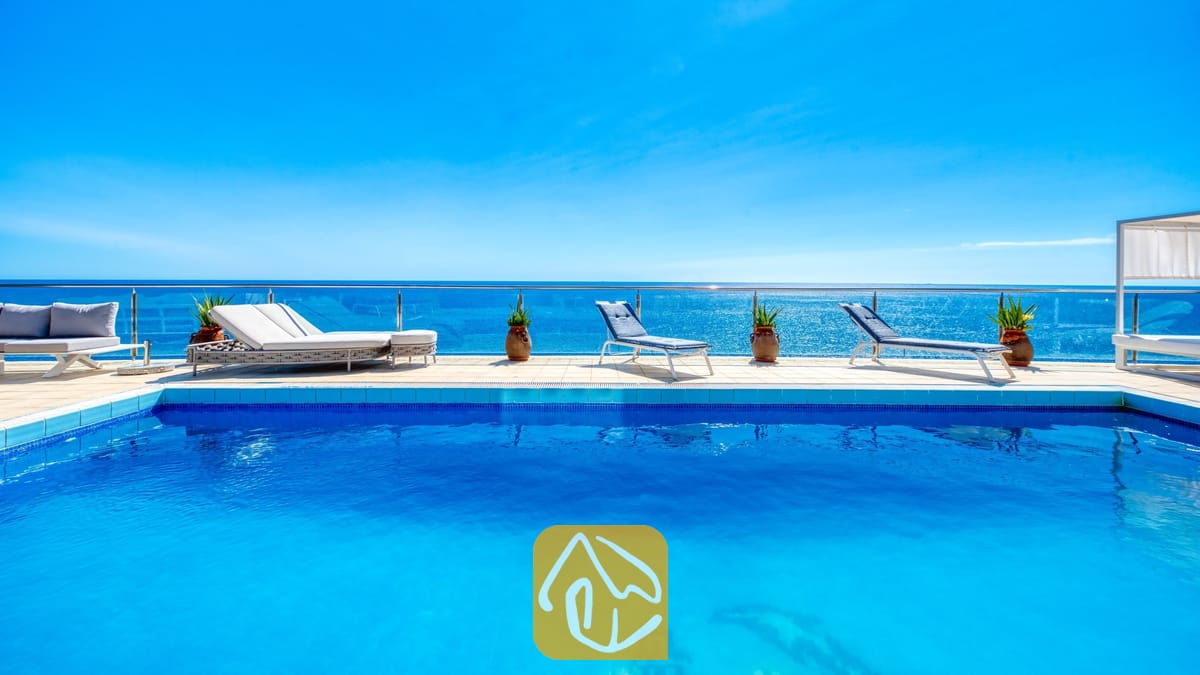Vakantievilla's Costa Brava Spanje - Villa Infinity - Helblauwe zwembad bij Villa Infinity met witte ligbedden en potplanten op het betegelde zwembadterras met uitzicht op zee
