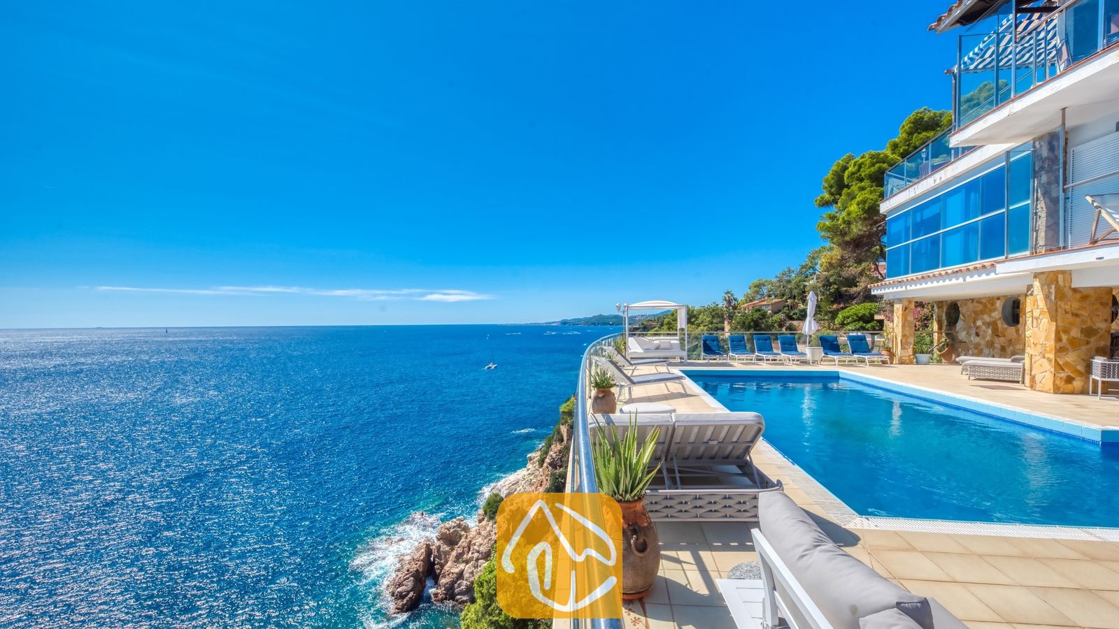 Vakantievilla's Costa Brava Spanje - Villa Infinity - Infinityzwembad op de klif bij Villa Infinity met blauwe ligstoelen en een weids uitzicht op zee onder een heldere, blauwe hemel