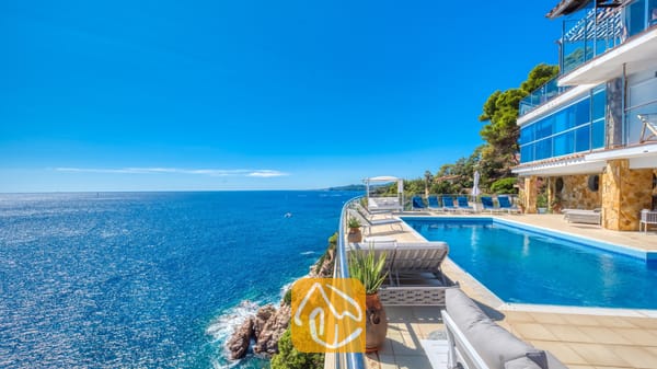 Vakantievilla's Costa Brava Spanje - Villa Infinity - Infinityzwembad op de klif bij Villa Infinity met blauwe ligstoelen en een weids uitzicht op zee onder een heldere, blauwe hemel