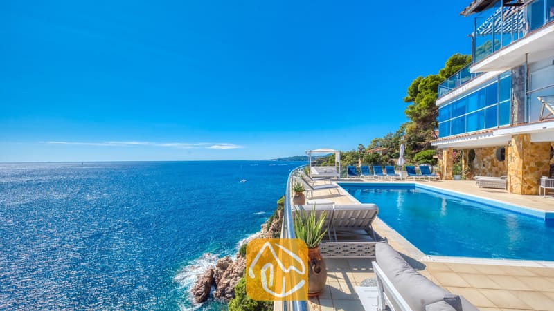 Vakantievilla's Costa Brava Spanje - Villa Infinity - Infinityzwembad op de klif bij Villa Infinity met blauwe ligstoelen en een weids uitzicht op zee onder een heldere, blauwe hemel