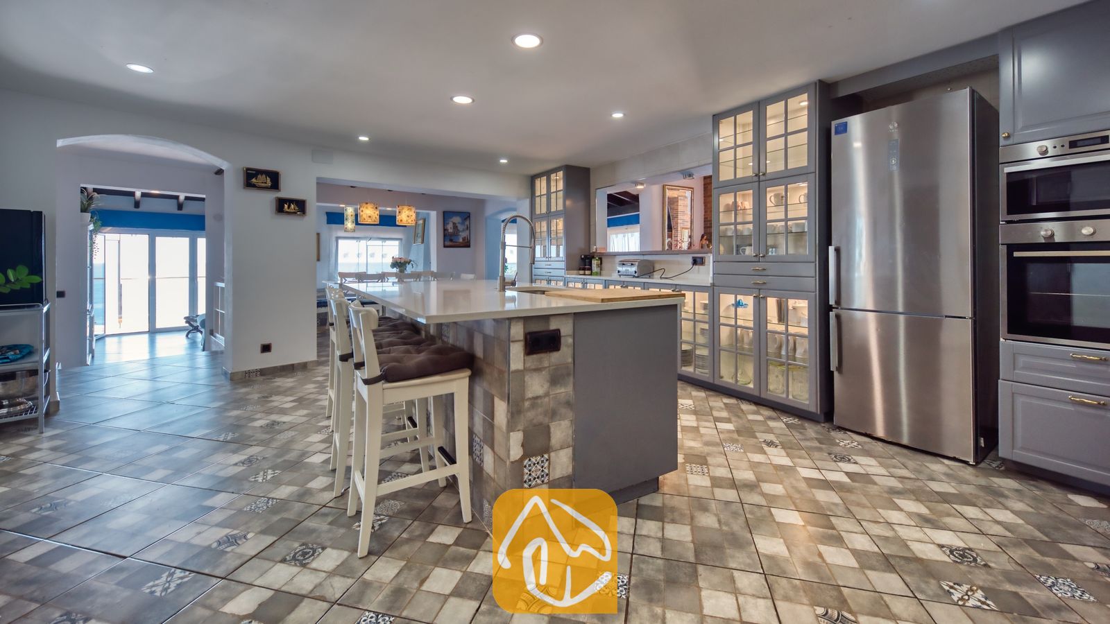 Vakantievilla's Costa Brava Spanje - Villa Infinity - Ruime keuken met een centraal kookeiland en barstoelen, grijze keukenkasten, een roestvrijstalen koelkast en een betegelde vloer met motief.