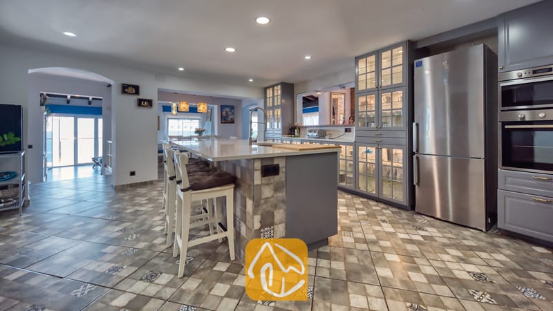 Villas de vacances Costa Brava Espagne - Villa Infinity - Spacieuse cuisine dotée d'un îlot central avec des tabourets de bar, de placards gris, d'un réfrigérateur en acier inoxydable et d'un sol en carrelage à motifs.