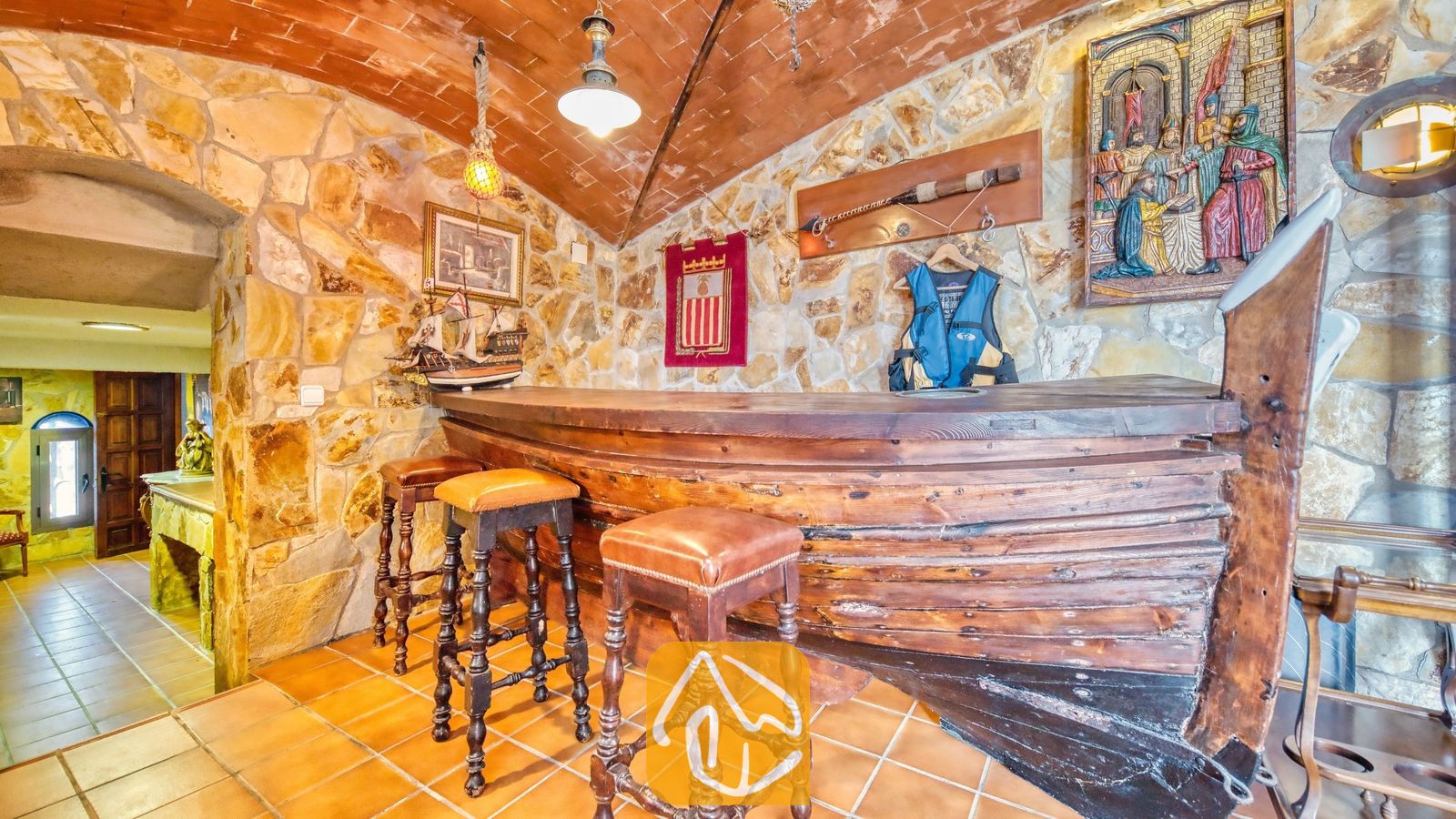 Vakantievilla's Costa Brava Spanje - Villa Infinity - Houten bar in de vorm van een boot met lederen krukken in Villa Infinity, voorzien van stenen muren, een bakstenen getoogd plafond en nautische decoraties.