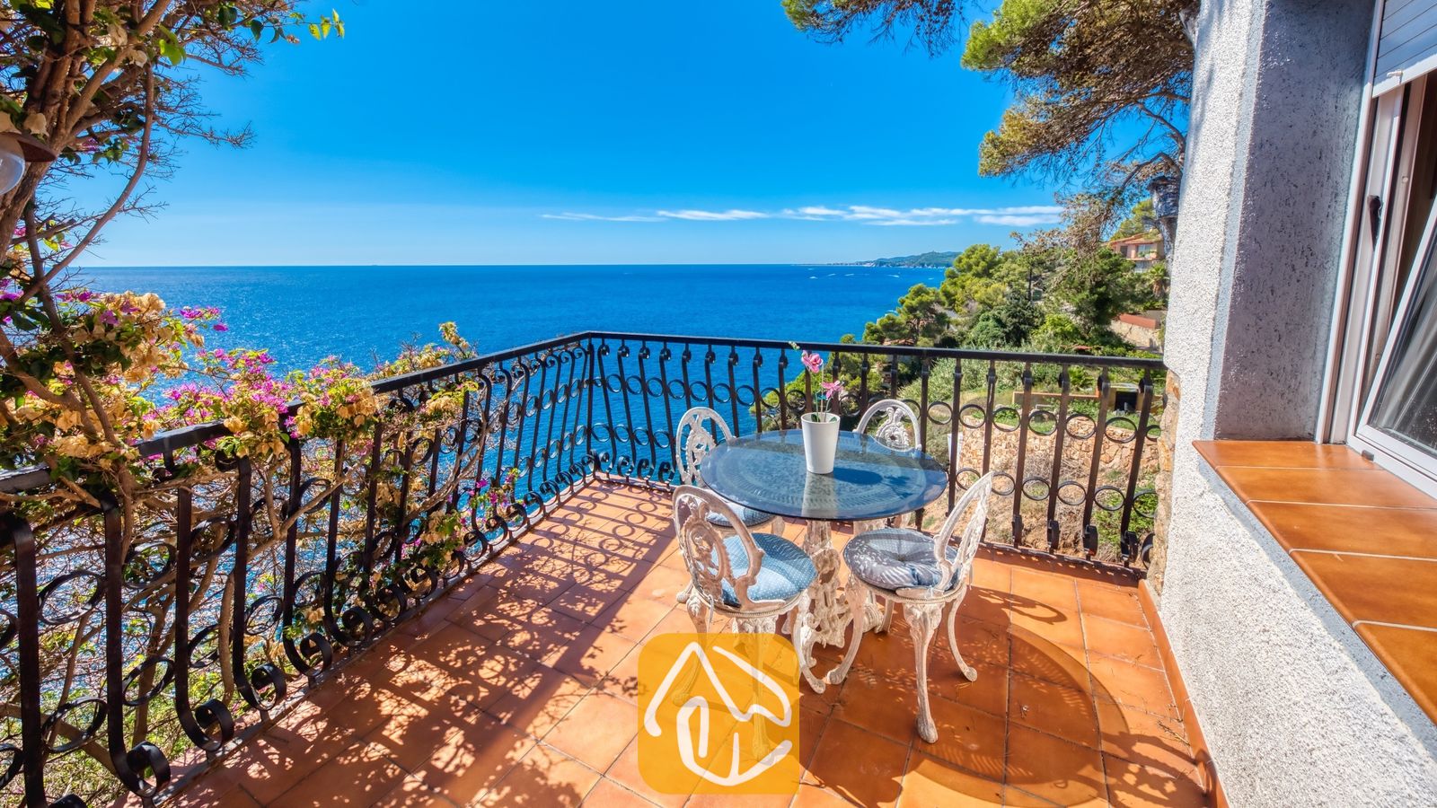 Vakantievilla's Costa Brava Spanje - Villa Infinity - Balkon met uitzicht op zee bij Villa Infinity, voorzien van een ronde glazen tafel met sierlijke witte metalen stoelen en terracotta vloertegels.