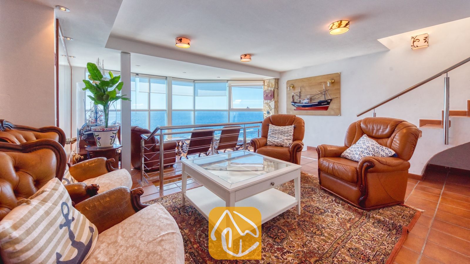 Vakantievilla's Costa Brava Spanje - Villa Infinity - Woonkamer van Villa Infinity met bruine lederen fauteuils, een witte salontafel en grote ramen met uitzicht op zee.
