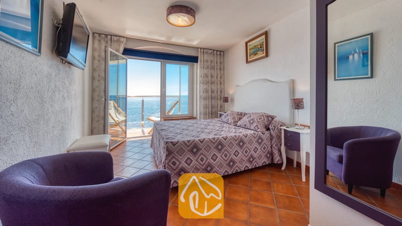 Villas de vacances Costa Brava Espagne - Villa Infinity - Chambre à la Villa Infinity avec un lit double, un couvre-lit violet à motifs et des portes vitrées coulissantes donnant sur un balcon avec vue sur la mer
