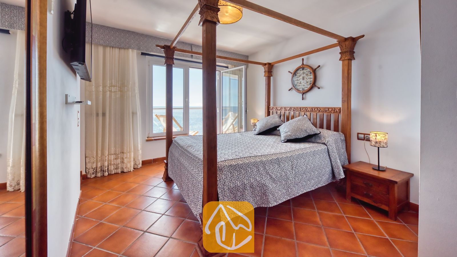 Vakantievilla's Costa Brava Spanje - Villa Infinity - Slaapkamer met houten hemelbed, gedessineerd beddengoed, tegelvloeren en een raam met uitzicht op zee.