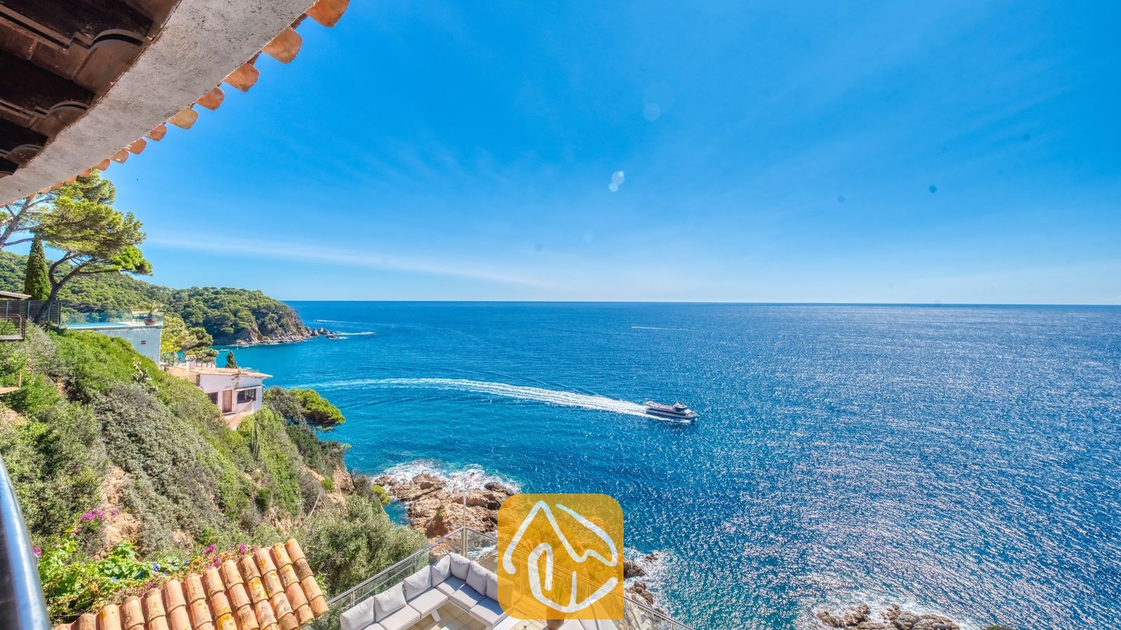 Vakantievilla's Costa Brava Spanje - Villa Infinity - Terras met uitzicht op de blauwe zee bij Villa Infinity, voorzien van een witte hoekbank en een langskomende boot op het water beneden