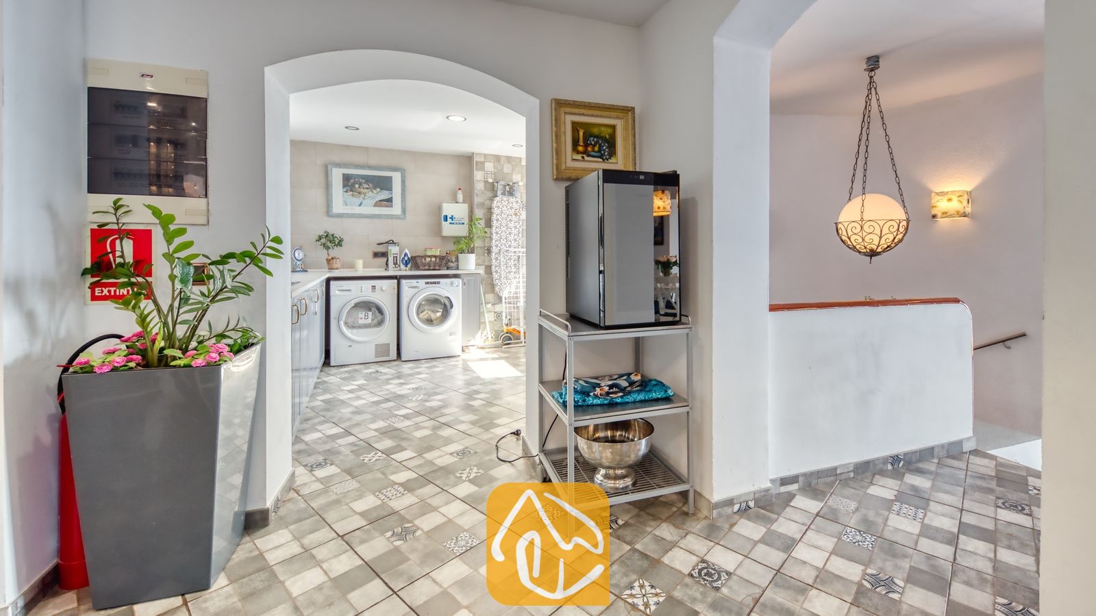 Vakantievilla's Costa Brava Spanje - Villa Infinity - Bijkeuken met twee wasmachines, te zien door een toogvormige deuropening, voorzien van betegelde vloeren met motief en een metalen opbergwagen met een kleine koelkast.