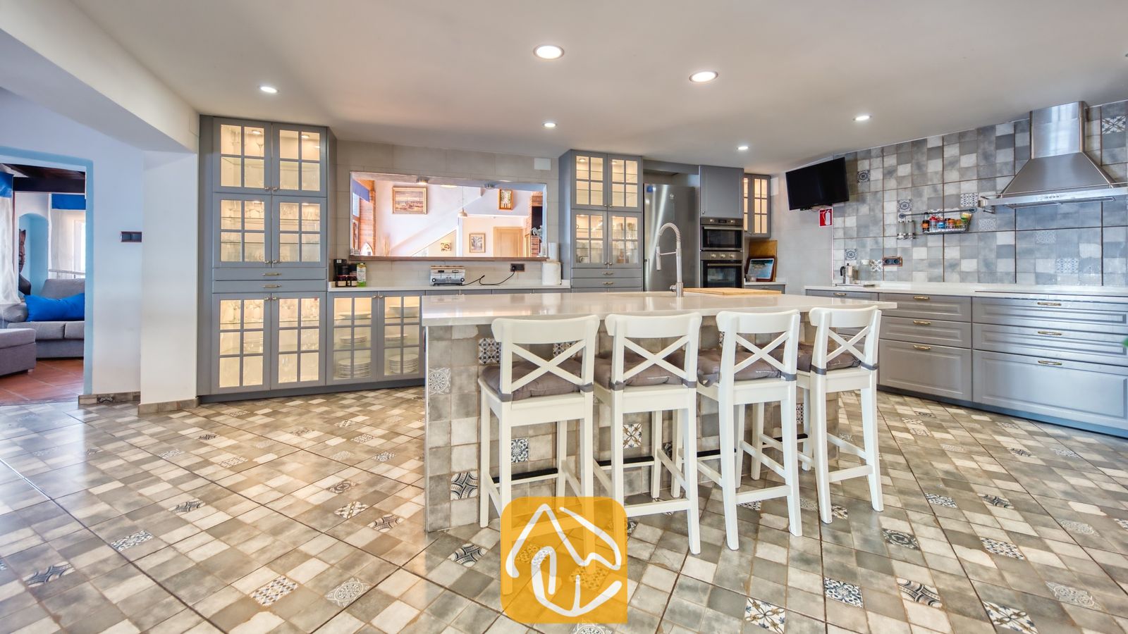 Vakantievilla's Costa Brava Spanje - Villa Infinity - Ruime keuken met grijze kasten, een betegelde vloer met motief en een kookeiland in het midden met vier witte barstoelen in Villa Infinity.