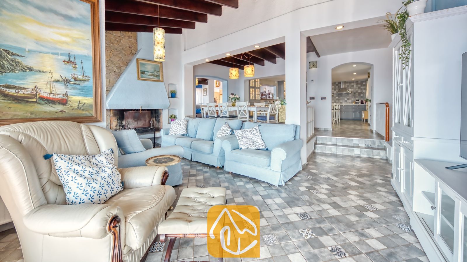 Vakantievilla's Costa Brava Spanje - Villa Infinity - Ruime woonkamer in Villa Infinity met gedessineerde tegelvloeren, lichtblauwe banken, een stenen open haard en donkere houten plafondbalken.