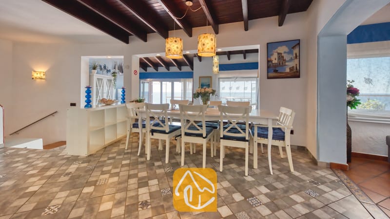 Villas de vacances Costa Brava Espagne - Villa Infinity - Coin repas doté d'une longue table blanche assortie à ses chaises, de poutres apparentes en bois foncé et d'un sol en carrelage à motifs à la Villa Infinity.