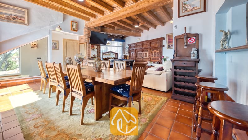 Villas de vacances Costa Brava Espagne - Villa Infinity - Vaste coin repas doté d'une grande table en bois et de chaises assorties, de poutres apparentes au plafond et d'un sol en carrelage en terre cuite à la Villa Infinity.