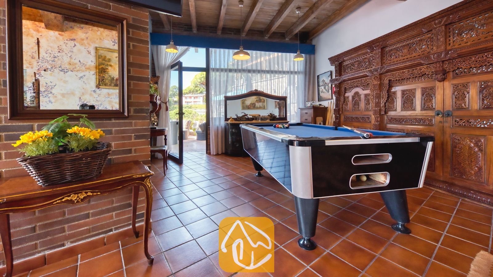 Vakantievilla's Costa Brava Spanje - Villa Infinity - Spelkamer in Villa Infinity met een blauwe biljarttafel, terracotta tegelvloer, zichtbare houten plafondbalken en een grote, sierlijk snijwerk houten wandkast.