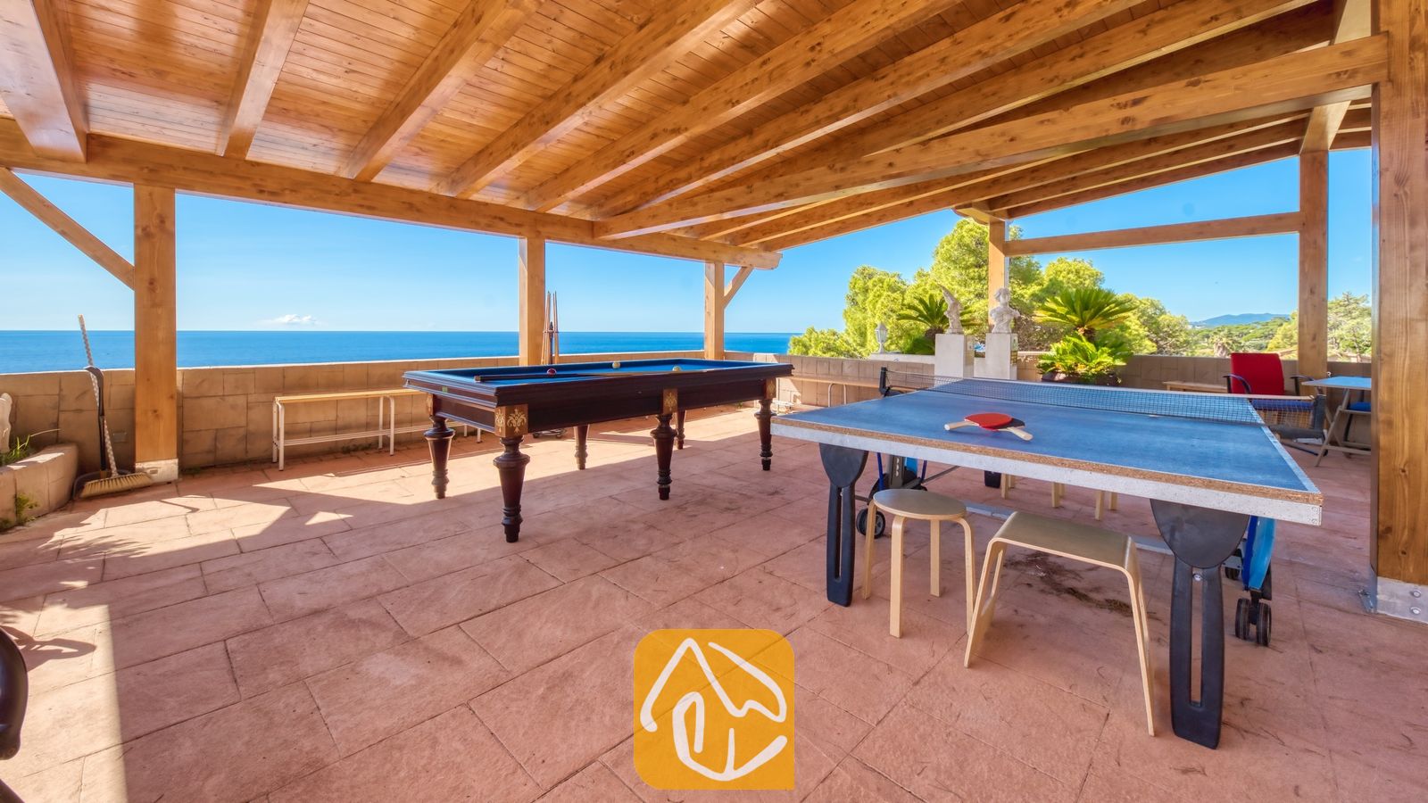 Vakantievilla's Costa Brava Spanje - Villa Infinity - Overdekt buitenbuitenterras bij Villa Infinity met een houten pergolaplafond, een biljarttafel en een blauwe tennistafel met uitzicht op zee.