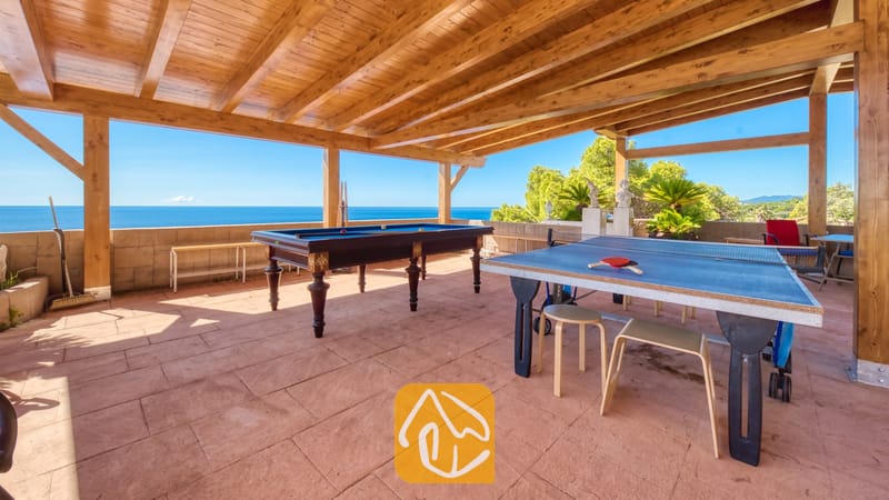 Villas de vacances Costa Brava Espagne - Villa Infinity - Terrasse extérieure couverte de la Villa Infinity dotée d'un plafond en pergola de bois, d'un billard et d'une table de ping-pong bleue, avec vue sur la mer.