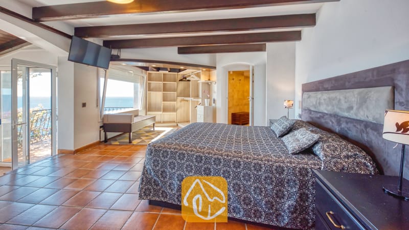 Villas de vacances Costa Brava Espagne - Villa Infinity - Chambre avec literie aux motifs sombres, poutres apparentes au plafond et sols en terre cuite à la Villa Infinity