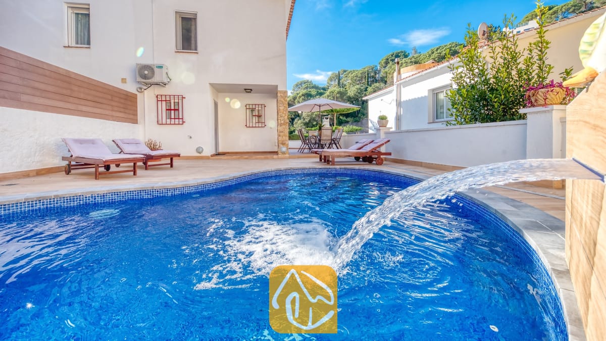 Vakantievilla's Costa Brava Spanje - Villa Blanca - Een gebogen, blauw getegeld zwembad met waterpartij bij Villa Blanca, voorzien van houten ligstoelen op het betegelde terras tegen een witte buitenmuur.