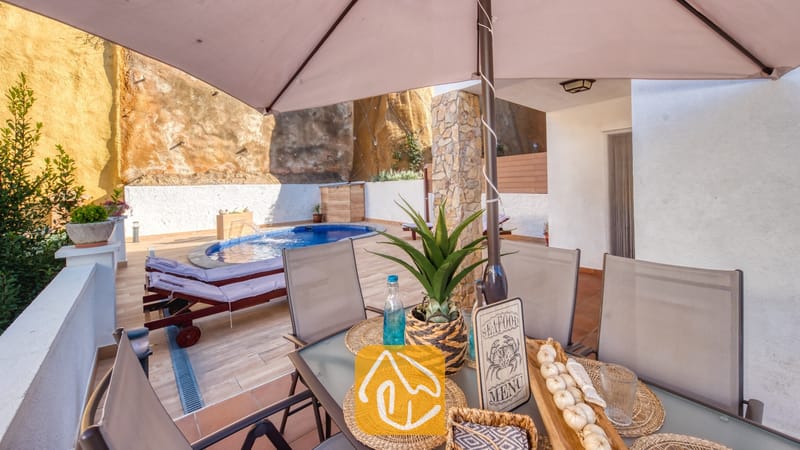 Vakantievilla's Costa Brava Spanje - Villa Blanca - Overdekte eettafel buiten met geweven placemats en een plant als middelpunt, met uitzicht op het zwembadterras en de ligstoelen van Villa Blanca.
