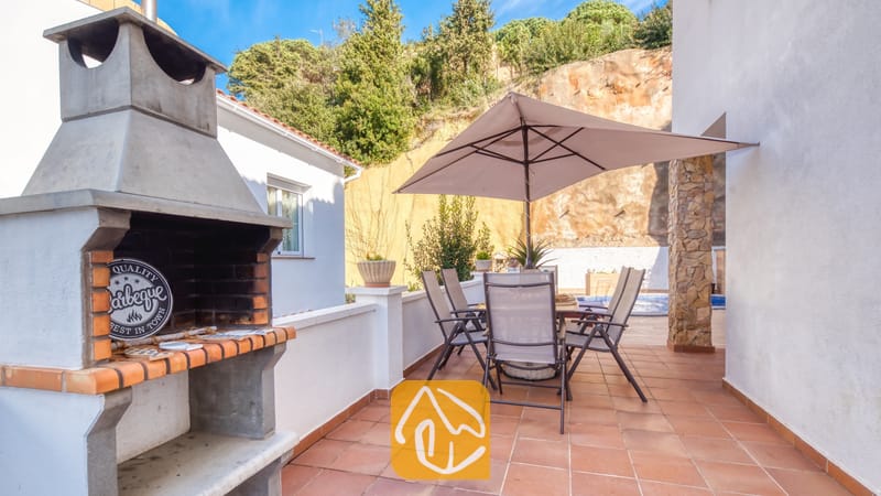 Vakantievilla's Costa Brava Spanje - Villa Blanca - Buitenbesterras van Villa Blanca met een stenen barbecue, een tuintafel met zes stoelen en een grote parasol op een tegelvloer.