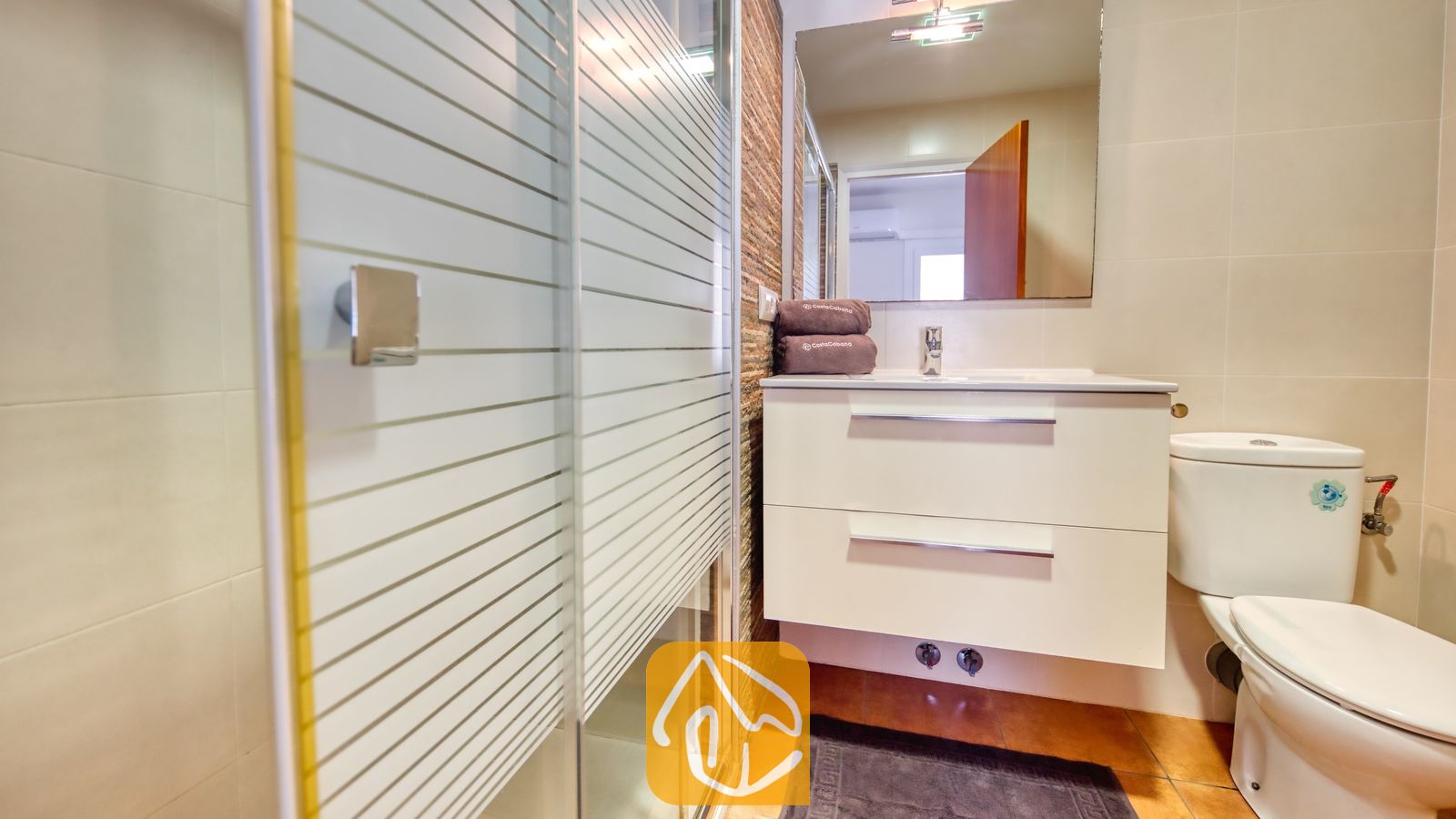 Vakantievilla's Costa Brava Spanje - Villa Blanca - Moderne badkamer met een glazen douchewand met horizontale, matglazen strepen, een wit wastafelmeubel met twee lades en een wandspiegel.