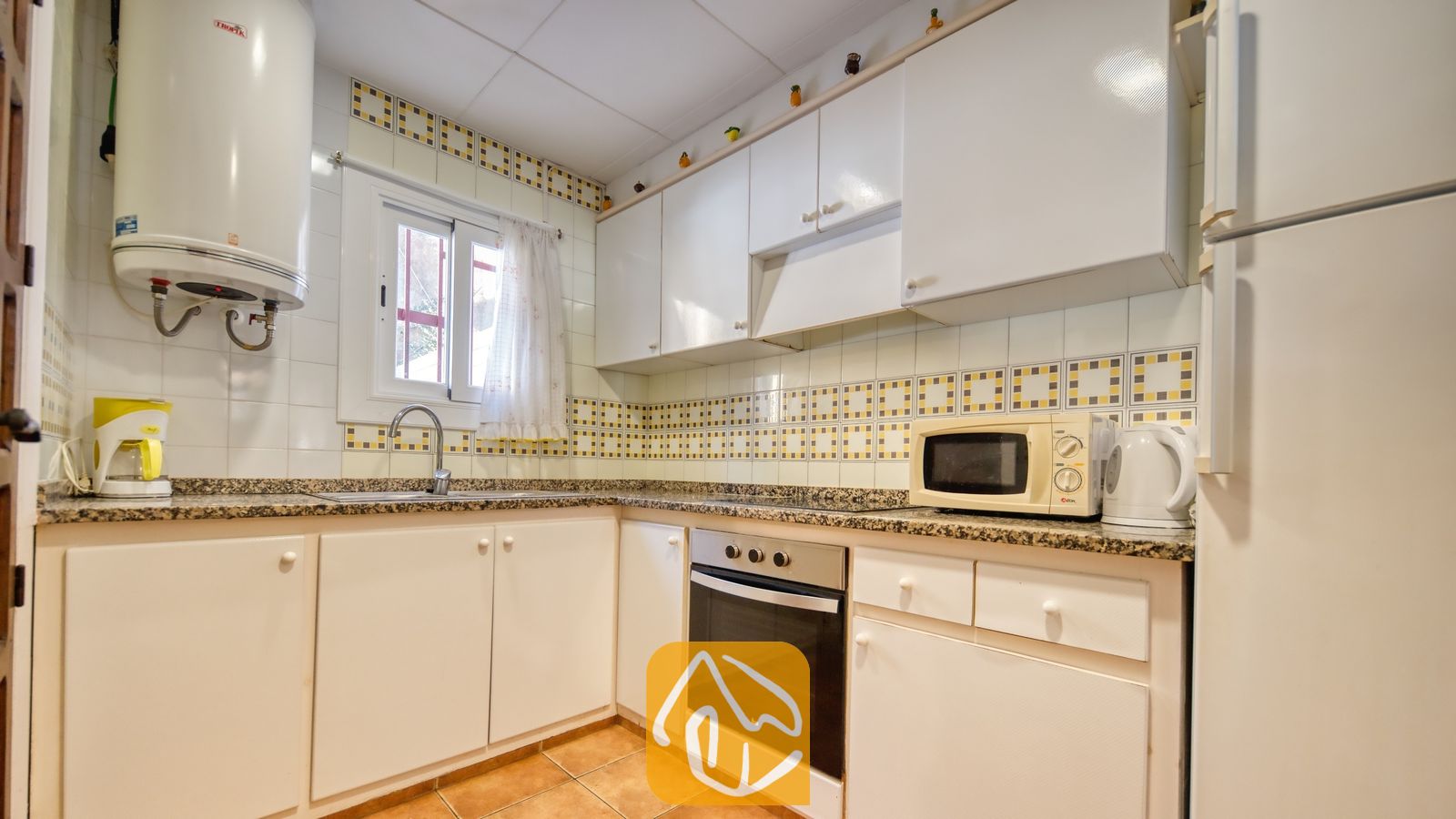 Vakantievilla's Costa Brava Spanje - Villa Blanca - Keuken voorzien van witte kasten, granieten aanrechtbladen, een inbouwoven en decoratieve gele tegels met een motief boven de gootsteen.